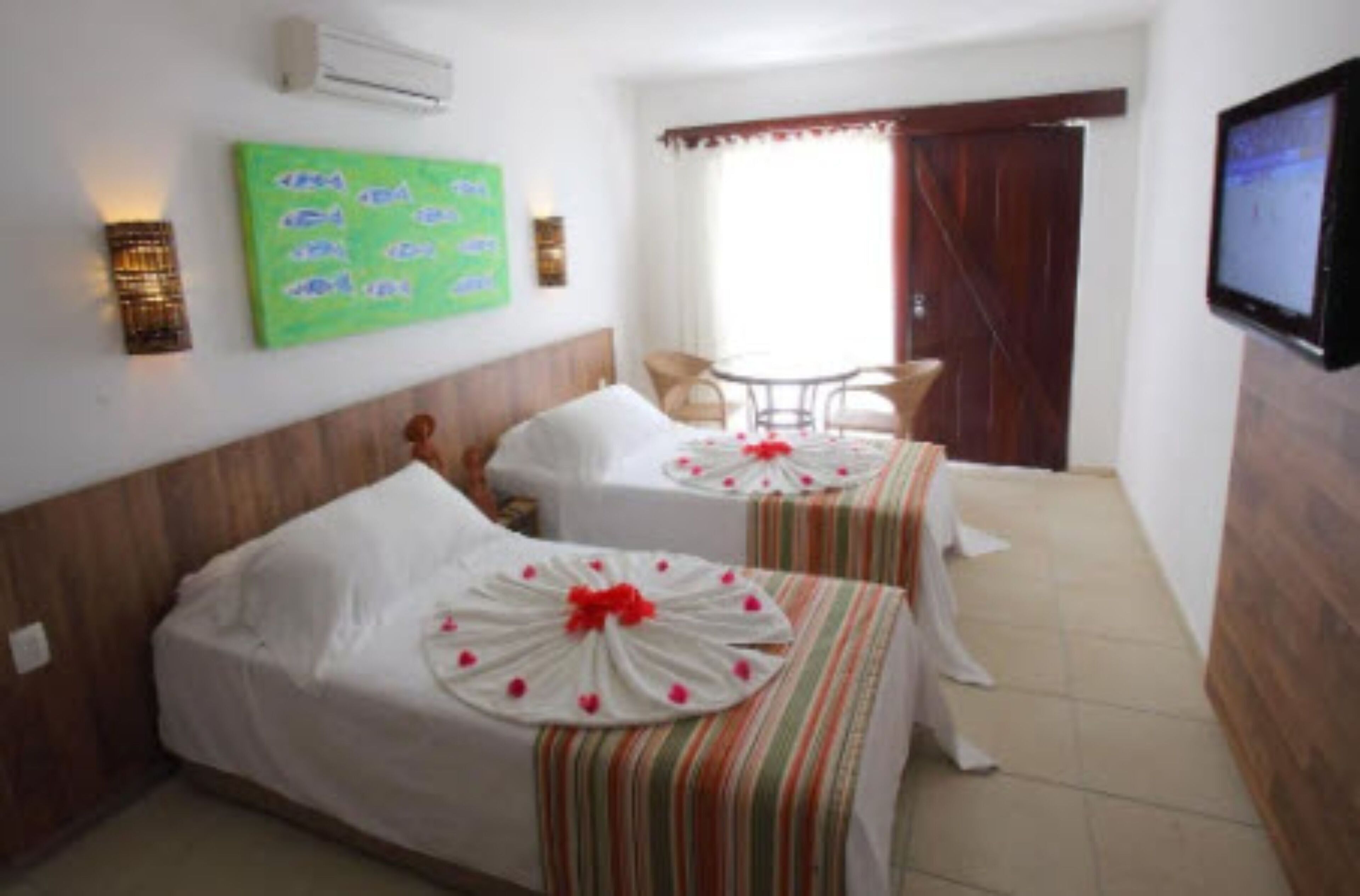 A hotel room with two beds, a TV, a window with curtains, and a small table with chairs.