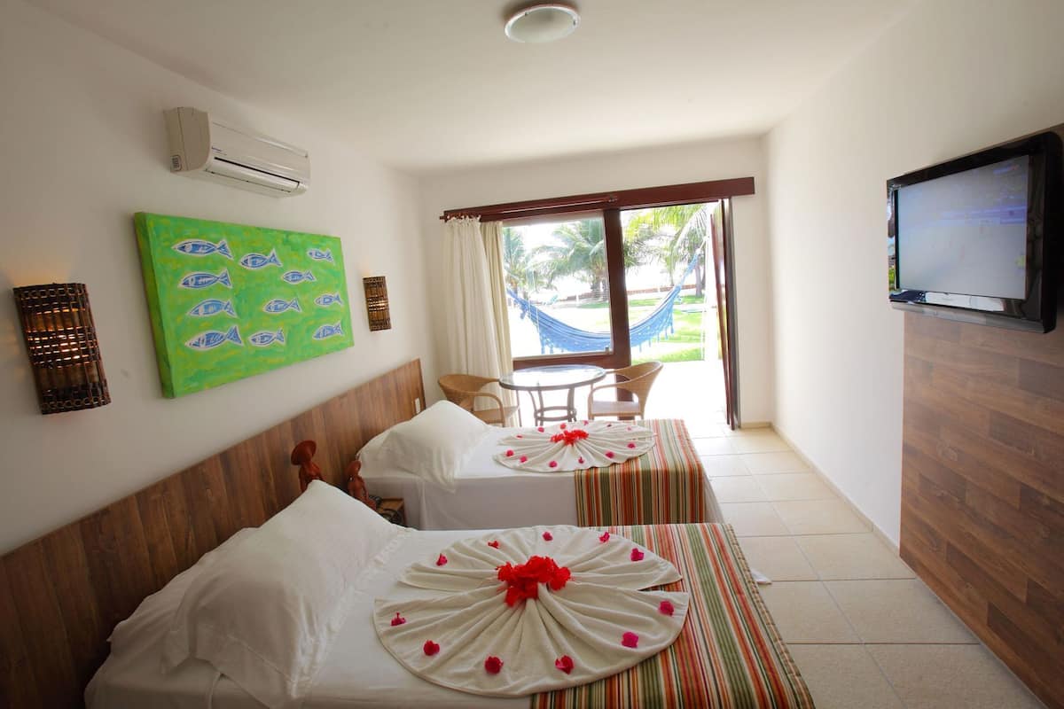 A hotel room with two beds, a TV, a hammock outside, and a view of greenery.