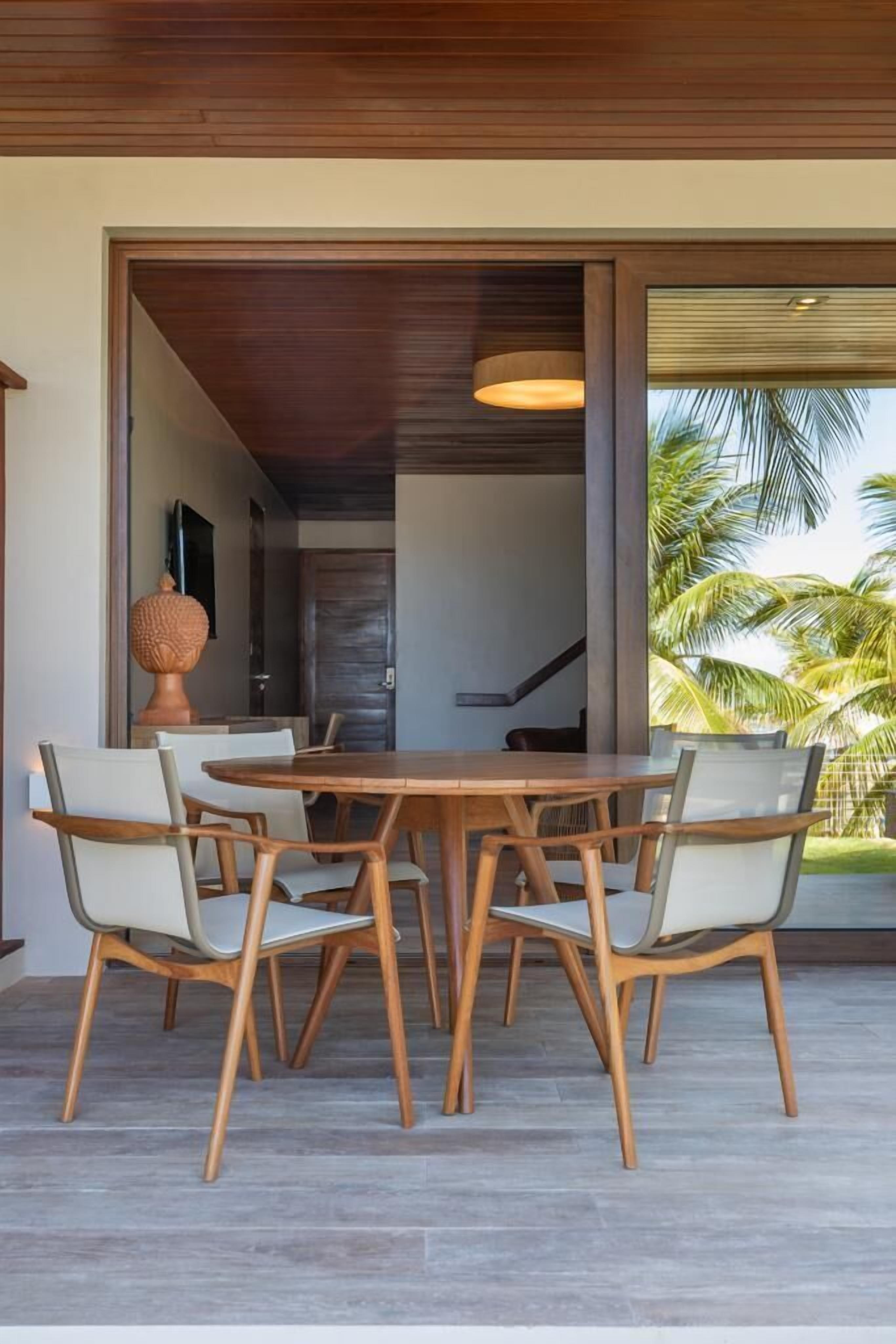 Un coin repas avec une table et des chaises en bois, un grand vase et une vue sur des palmiers.