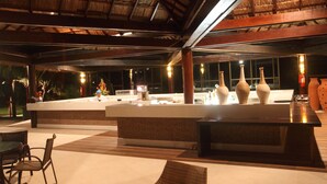 An outdoor bar area with wicker furniture, a counter with vases, and a thatched roof structure. - Serrambi Resort (Ipojuca)
