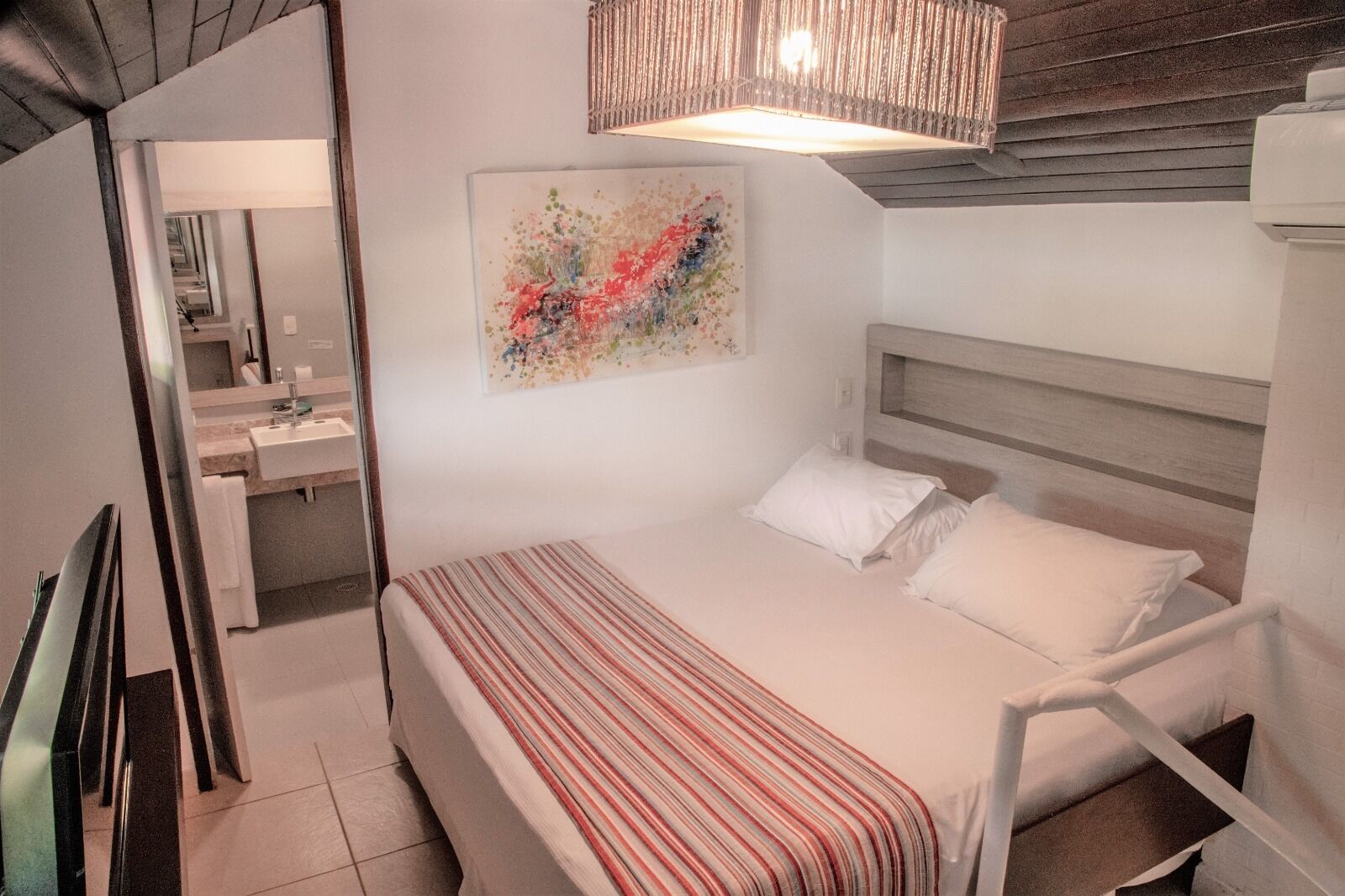 A bedroom with a bed, a bedside table, a mirror, and a hanging light fixture.