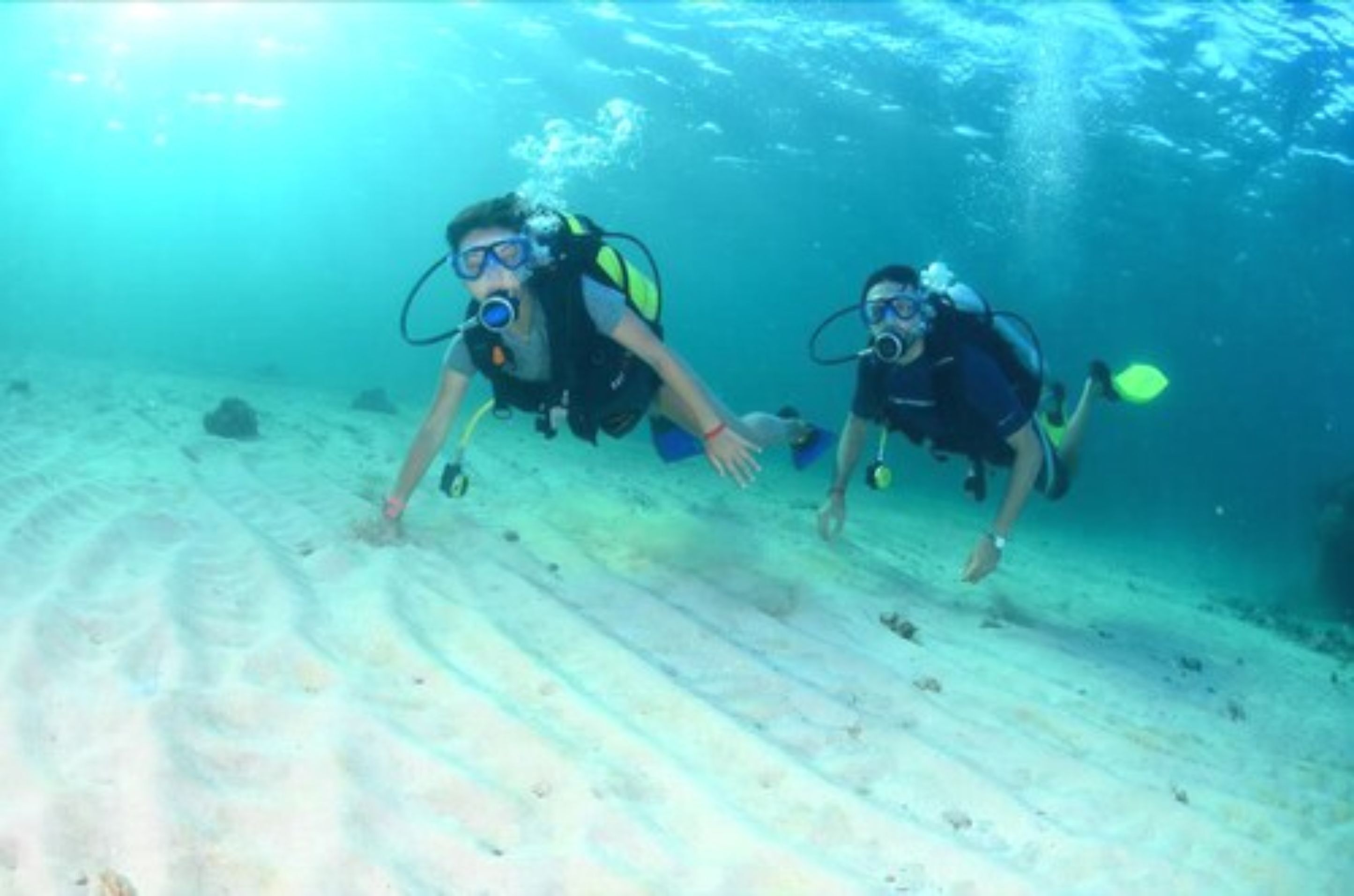Two scuba divers underwater with fins and oxygen tanks.