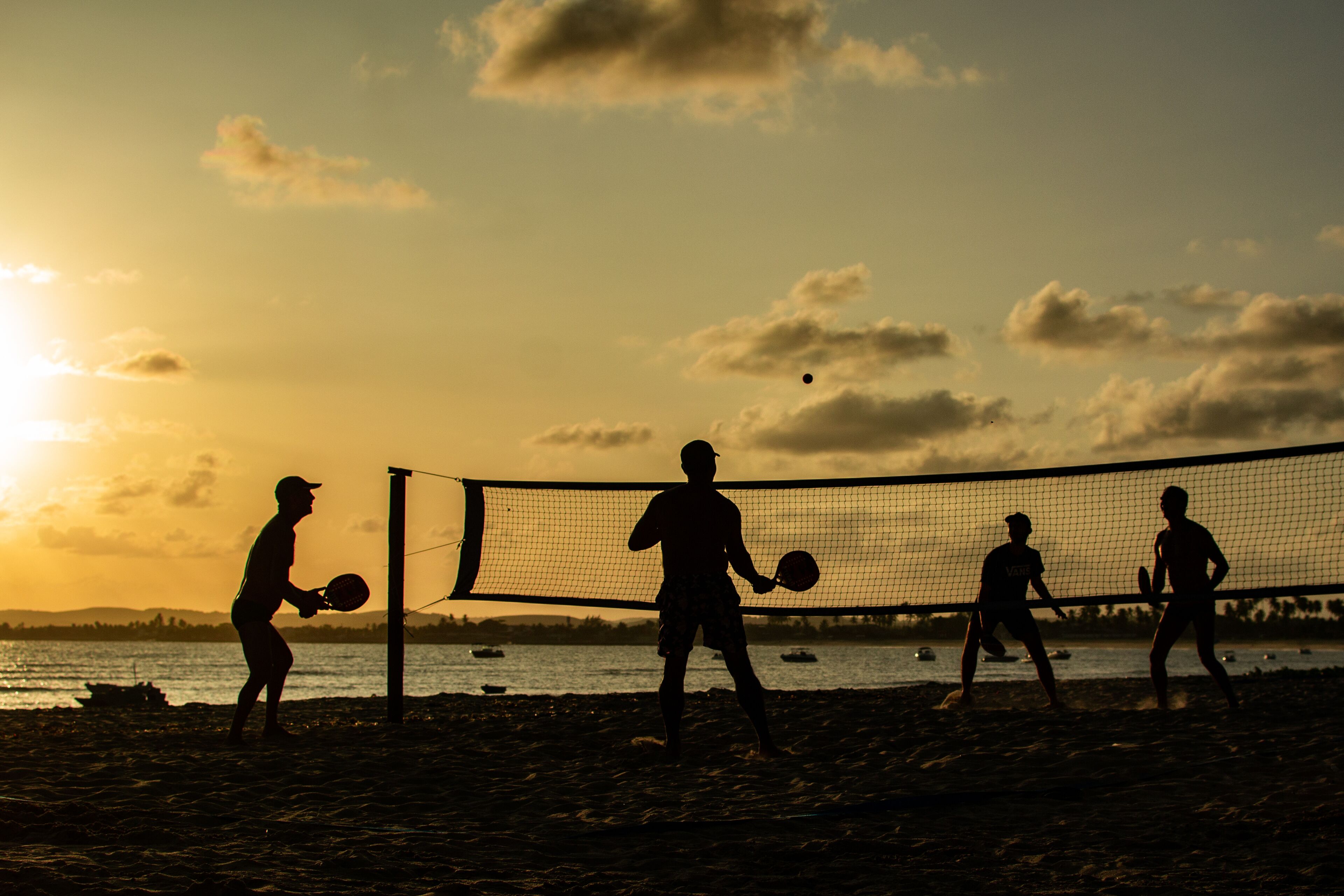 Un partido de voleibol de playa al atardecer, con siluetas de jugadores contra el cielo.