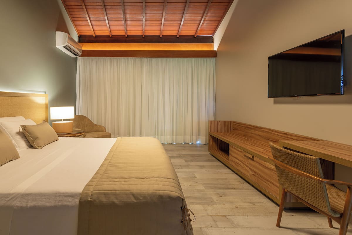 A hotel room with a bed, bedside table, lamp, TV, and a wooden console table.