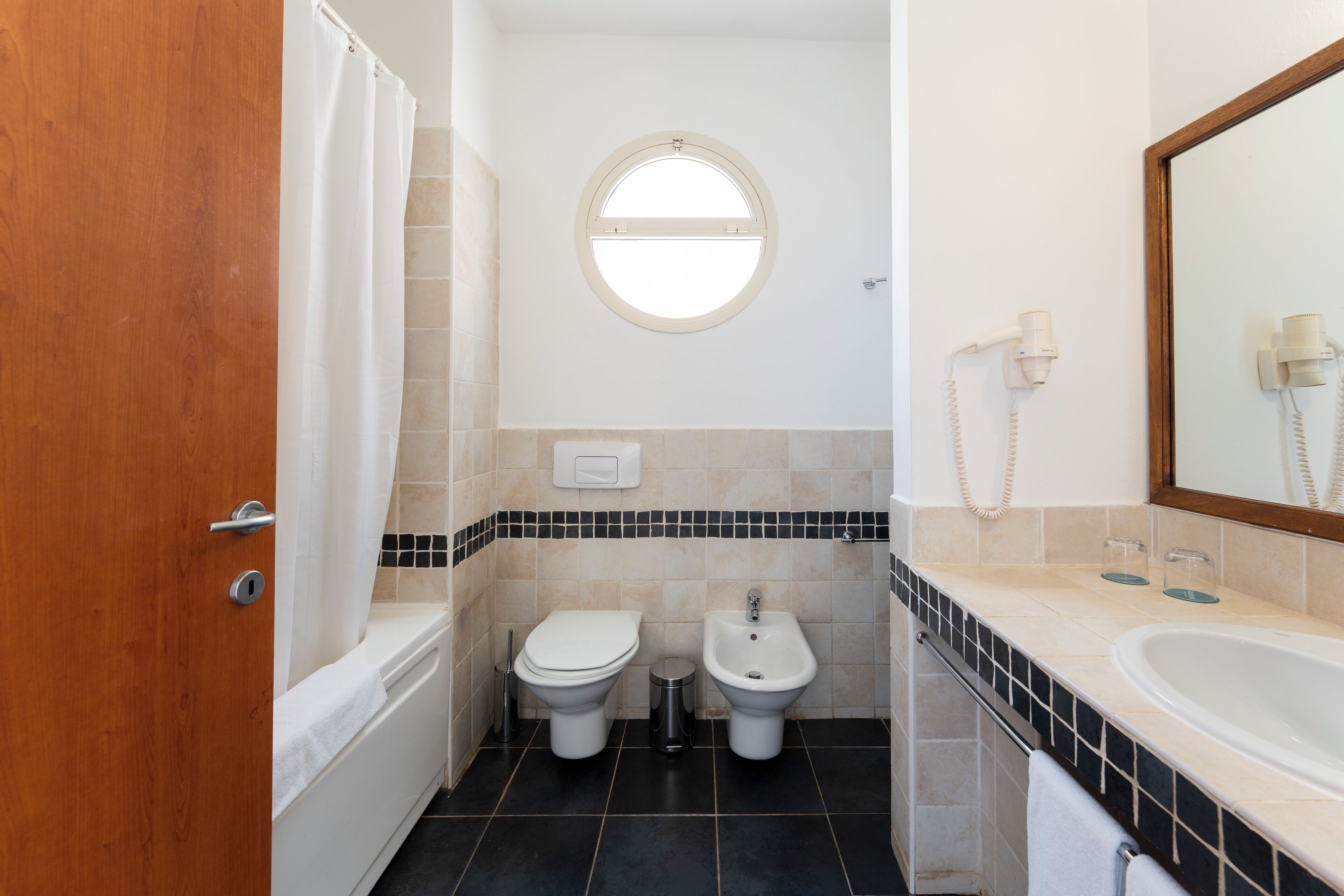 Un baño con bañera, dos inodoros, un bidé, lavamanos, espejo y teléfono.