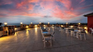 An outdoor seating area with tables and chairs, overlooking a body of water, under a twilight sky. - Occidental Boa Vista Beach (Boa Vista)