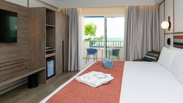 A hotel room with a bed, a TV, a minibar, a balcony with a view, and a dining area.