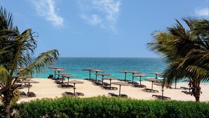 A beach with rows of sun loungers and umbrellas, palm trees, and the ocean in the background. - Occidental Boa Vista Beach (Boa Vista)