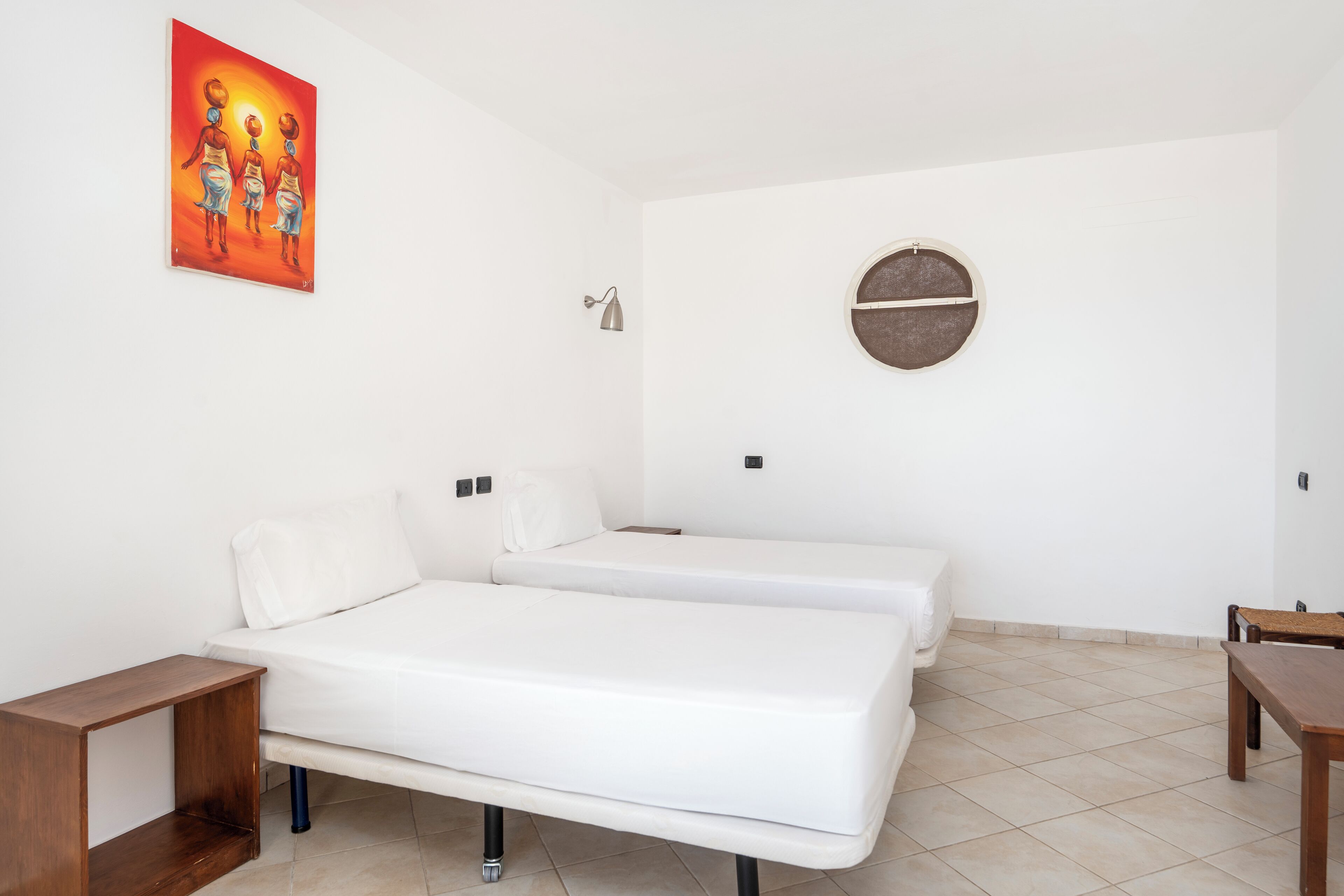 A room with two beds, a round wall decoration, a small table, and a painting on the wall.