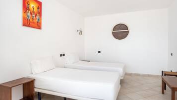 A room with two beds, a round wall decoration, a small table, and a painting on the wall.