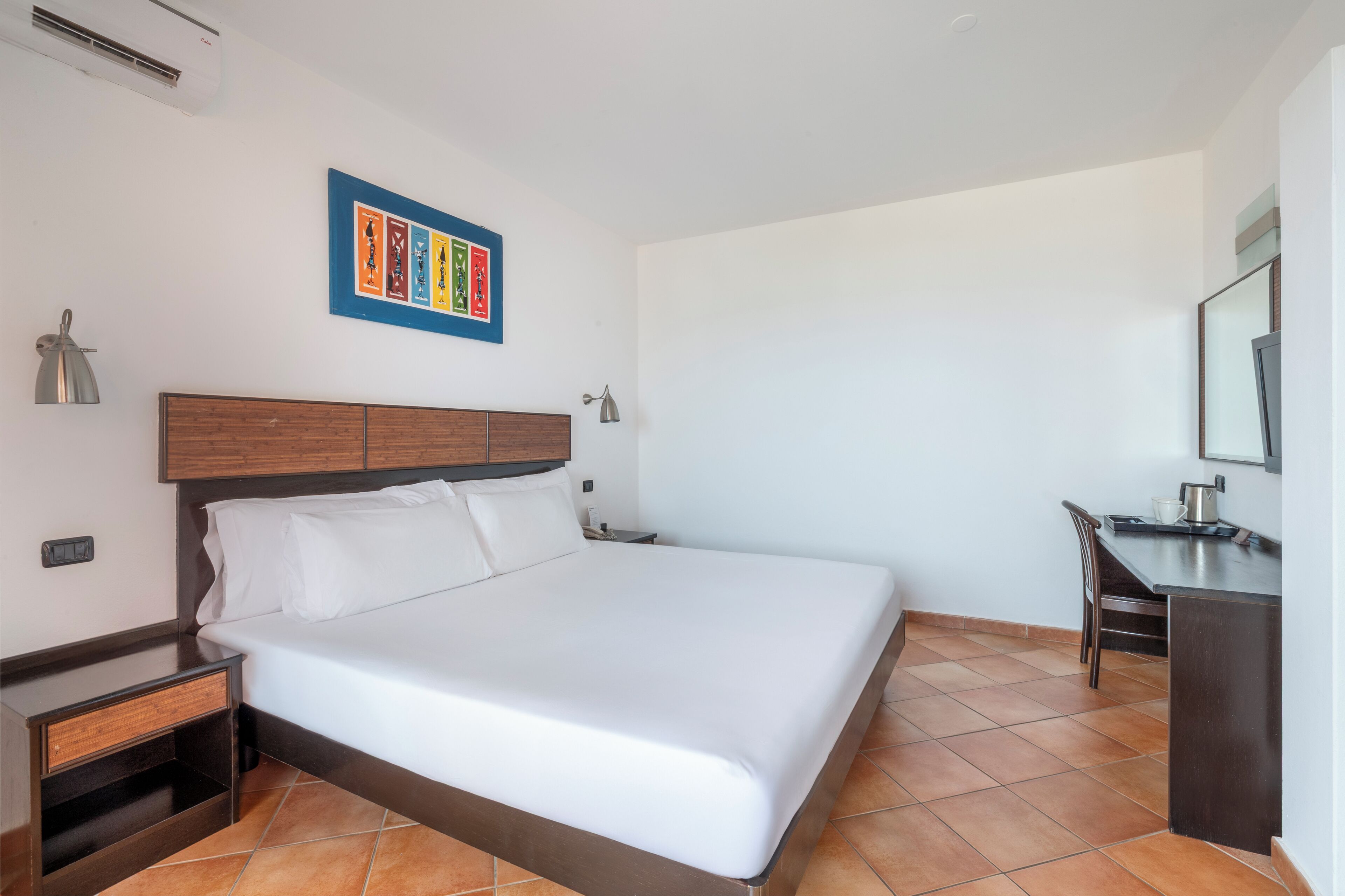 A hotel room with a large bed, a wooden headboard, a desk with a chair, and a small cabinet.
