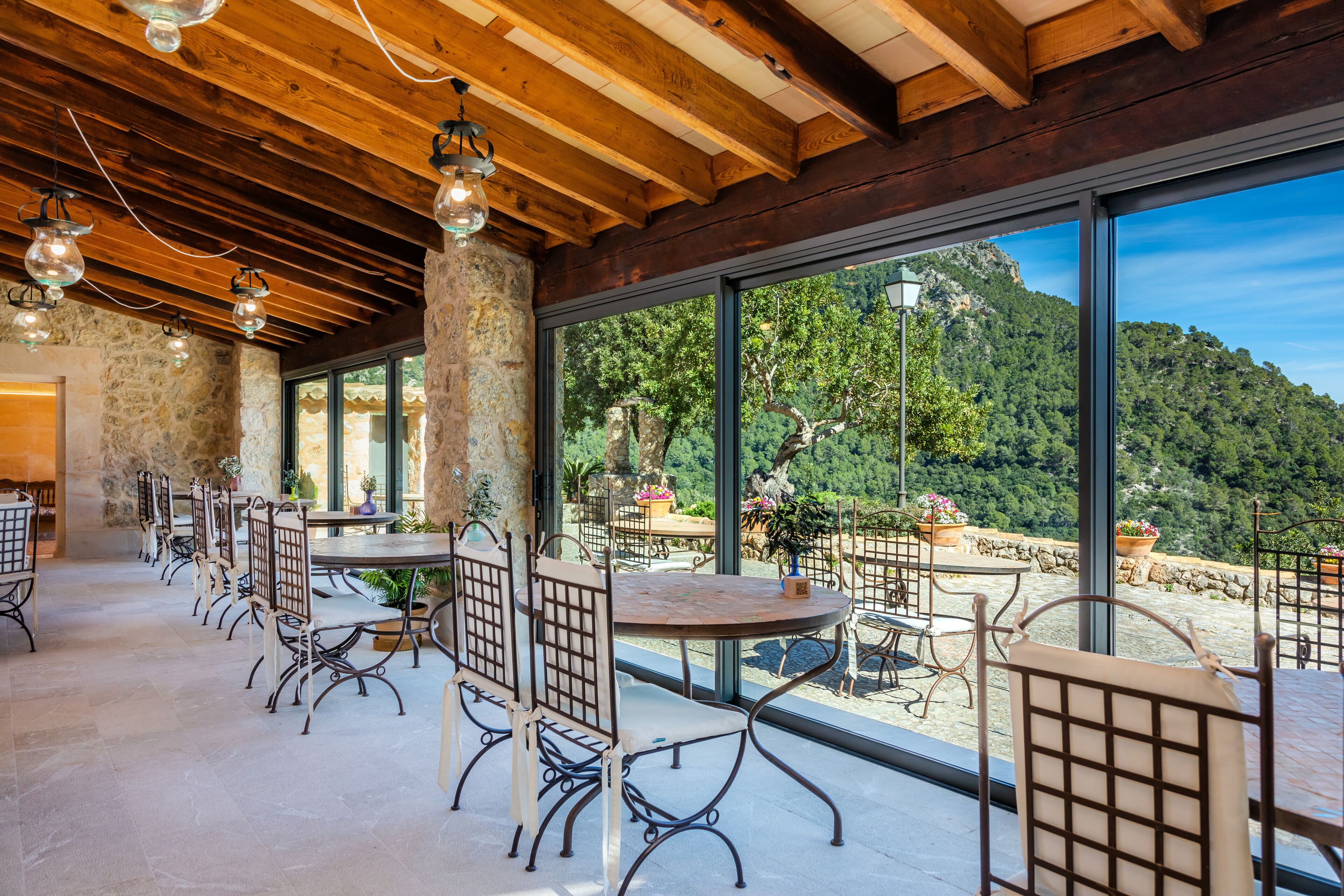 Un amplio comedor al aire libre con paredes de piedra y grandes ventanales que ofrecen vistas a un paisaje montañoso.