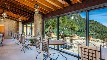 Un amplio comedor al aire libre con paredes de piedra y grandes ventanales que ofrecen vistas a un paisaje montañoso.