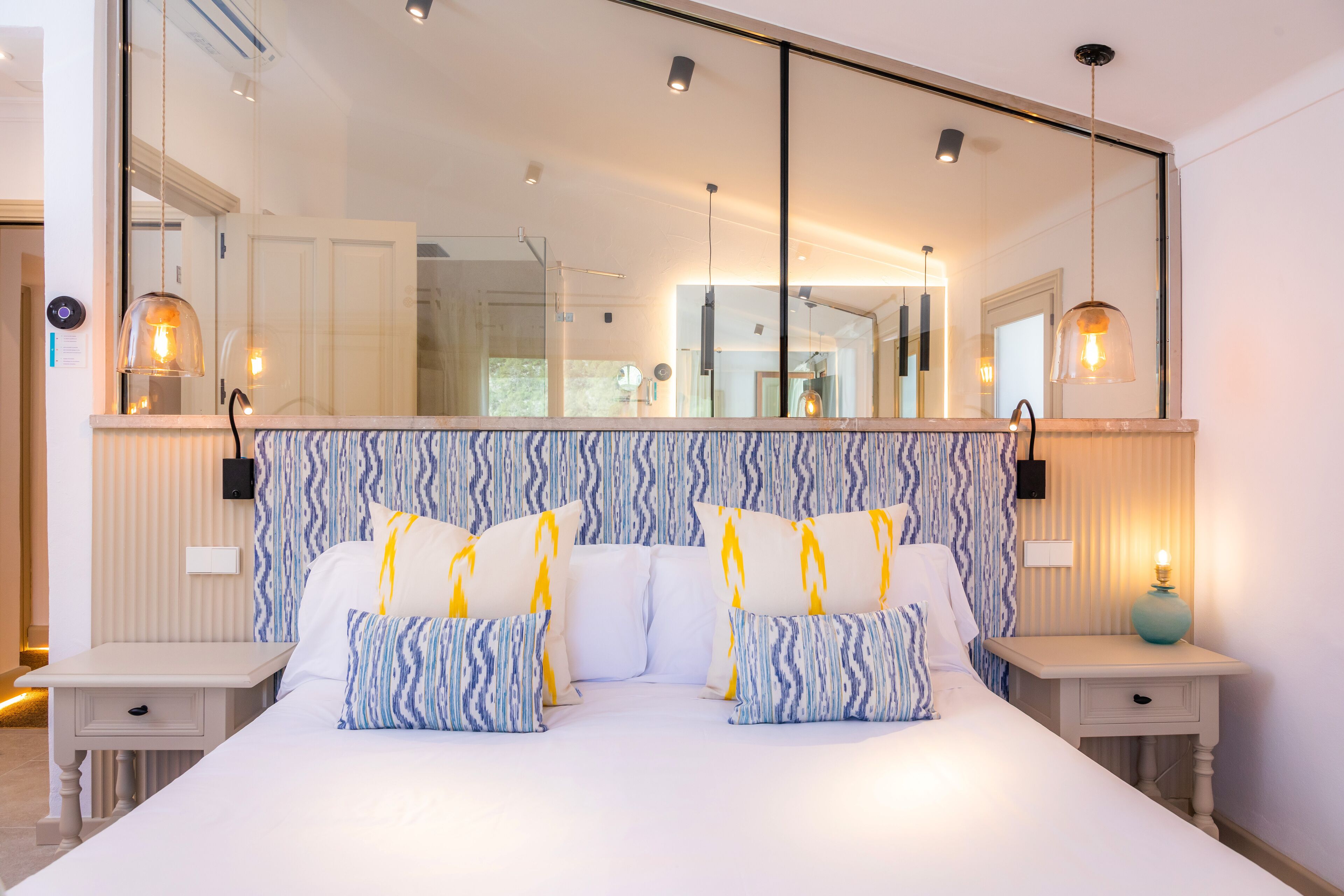 Een moderne hotelkamer met een groot bed, twee nachtkastjes, een spiegel en een wandlamp.