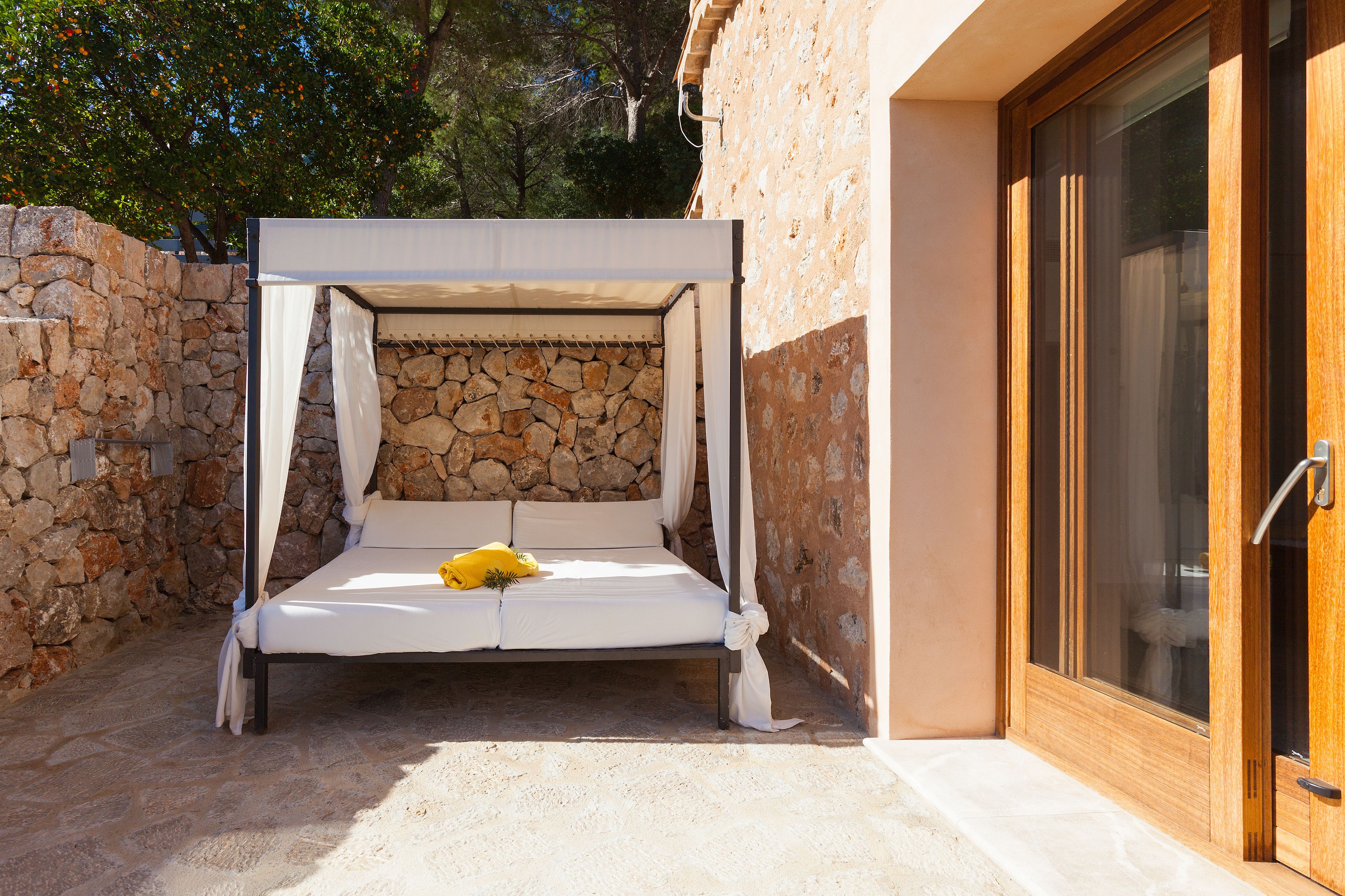 A stone-walled outdoor bedroom with a canopy bed, a stone wall, and a wooden door.