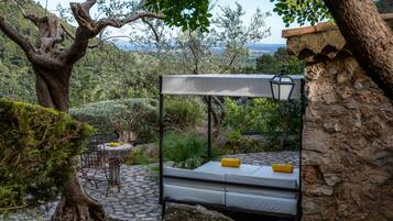 Un dormitorio rústico al aire libre con estructura de cama metálica, una mesita con sillas y un farol.