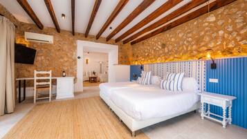 Un dormitorio con pared de piedra, vigas de madera, una cama, una mesita de noche, un escritorio y una silla.