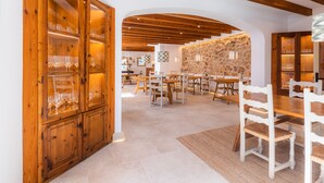 Un comedor espacioso con mesas y sillas de madera, una pared de piedra y un mueble de madera con puertas de cristal.
