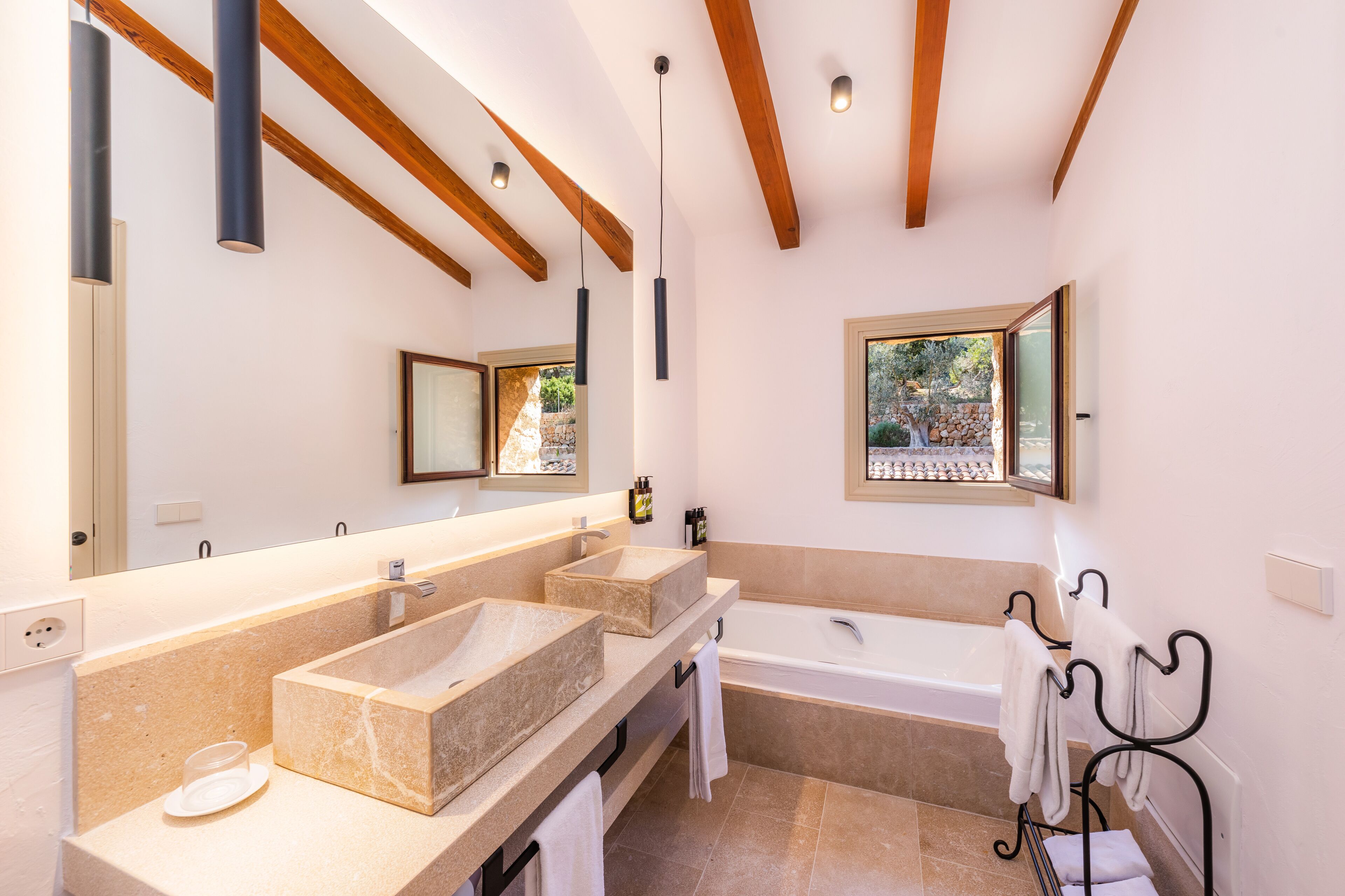 A modern bathroom with two sinks, a bathtub, wooden beams, and a large mirror.