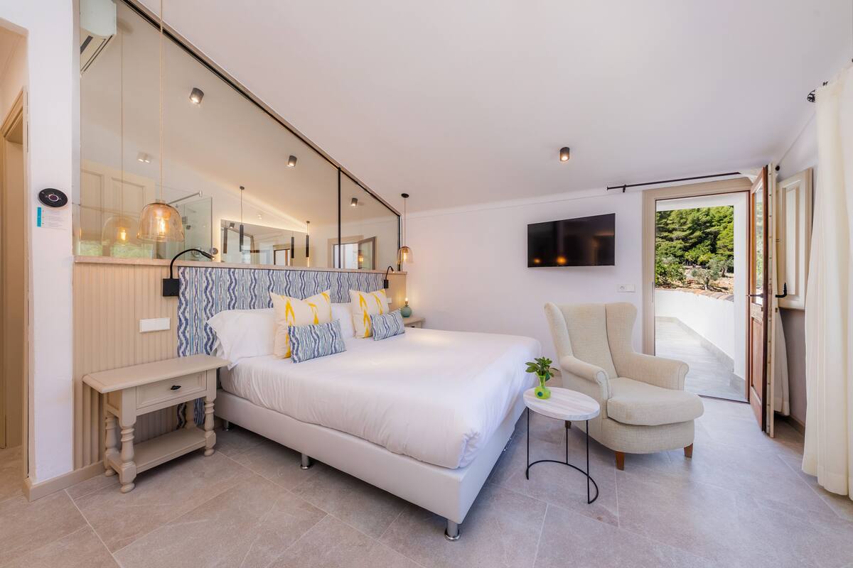 Ein modernes Schlafzimmer mit einem großen Bett, einem Nachttisch, einem Sessel, einem Fernseher und einem Balkon.