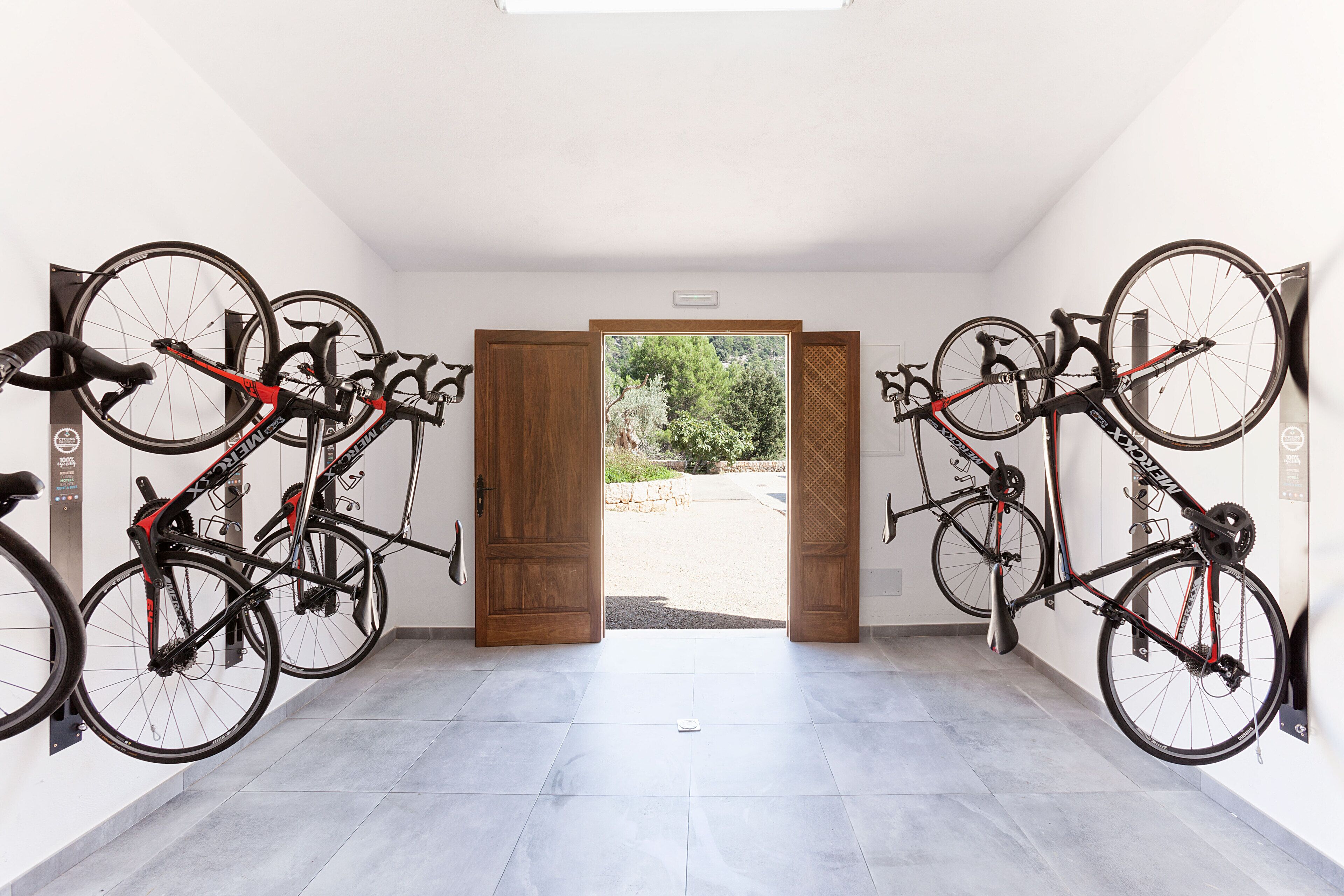 A room with bicycles mounted on the wall, a wooden door leading outside, and a tiled floor.