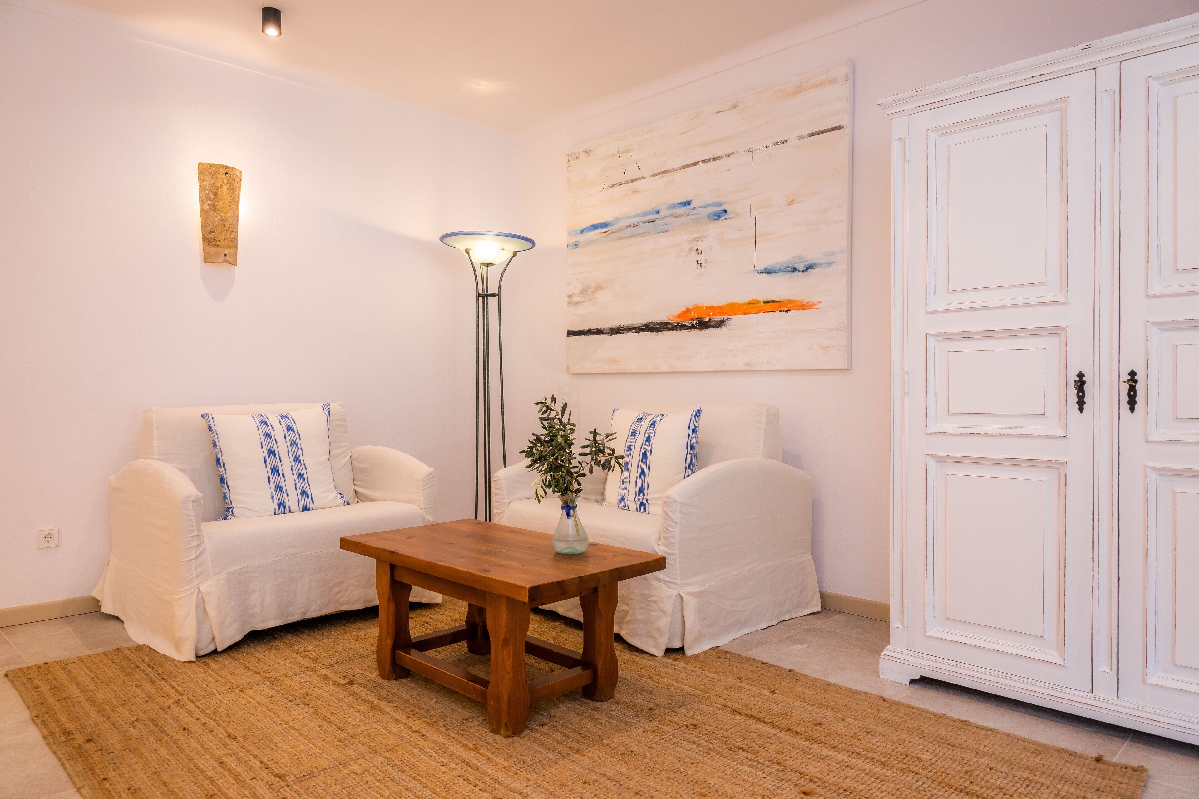 En stue med to hvide sofaer, et træsofabord, en gulvlampe, et billede og en hvid garderobe.