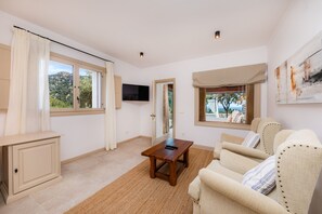 Un salón amplio con un gran ventanal, un televisor de pantalla plana, una mesa de centro de madera y un sofá color beige con almohadones a rayas.