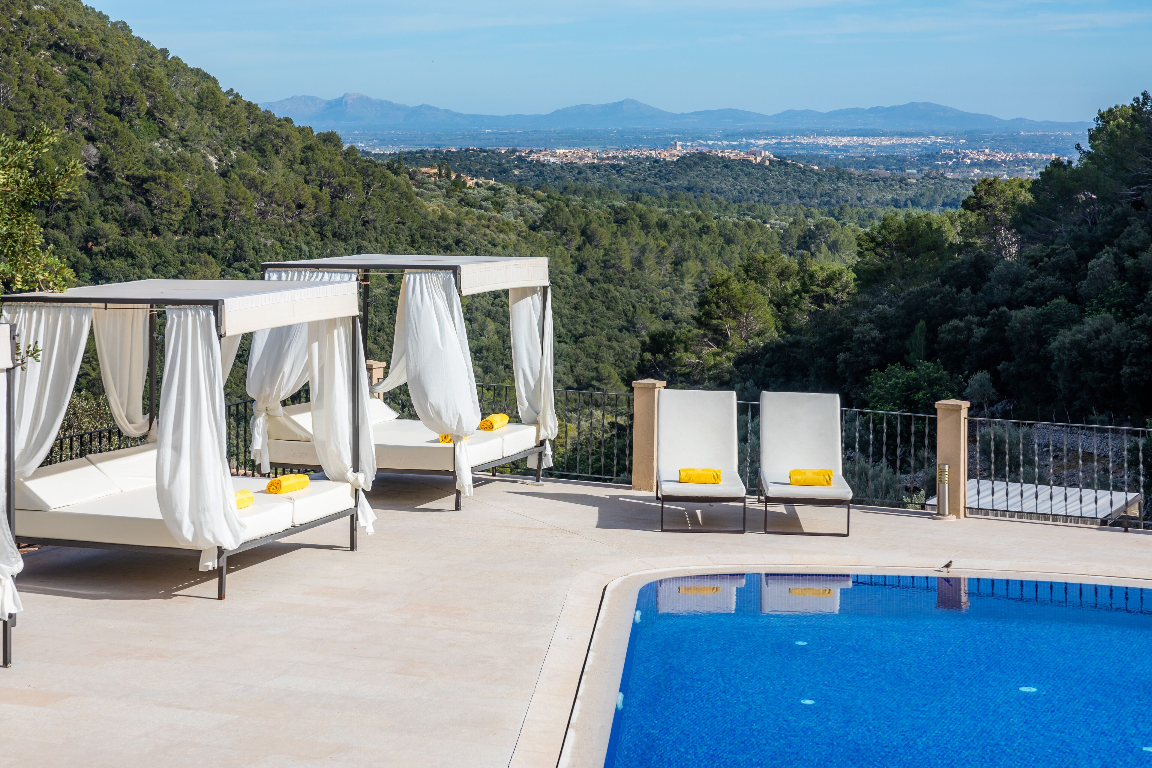 Un espace aménagé autour d’une piscine, offrant une vue sur la ville et les montagnes en arrière-plan.