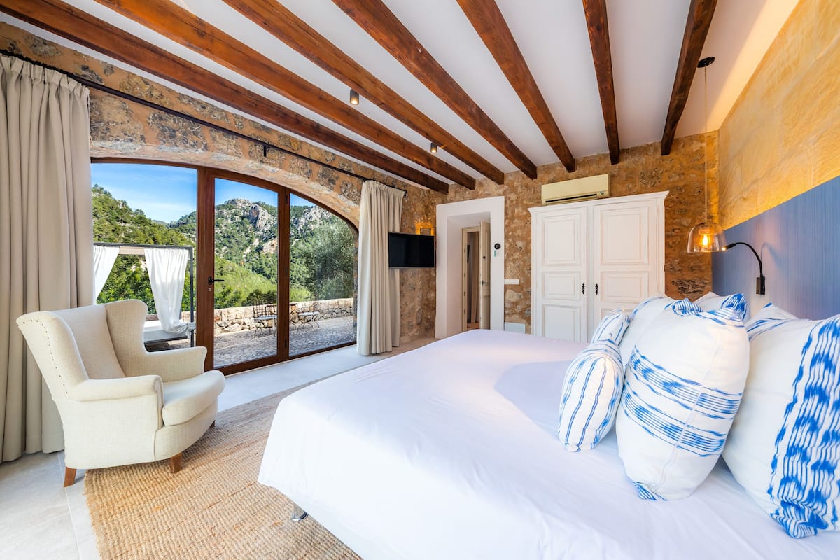 Ein Schlafzimmer mit einem großen Bett, einem Sessel und Blick ins Freie.