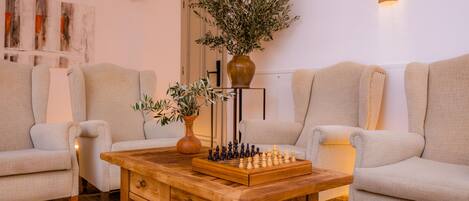A living room with two beige sofas, a wooden coffee table with a chessboard, and two potted plants.