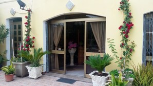 A building entrance with a glass door, potted plants, and a tiled patio. - Hotel Eliseo (Giardini Naxos)