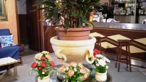 A bar area with a large potted plant, a round table with floral centerpieces, and a bar counter with various bottles. - Hotel Eliseo (Giardini Naxos)