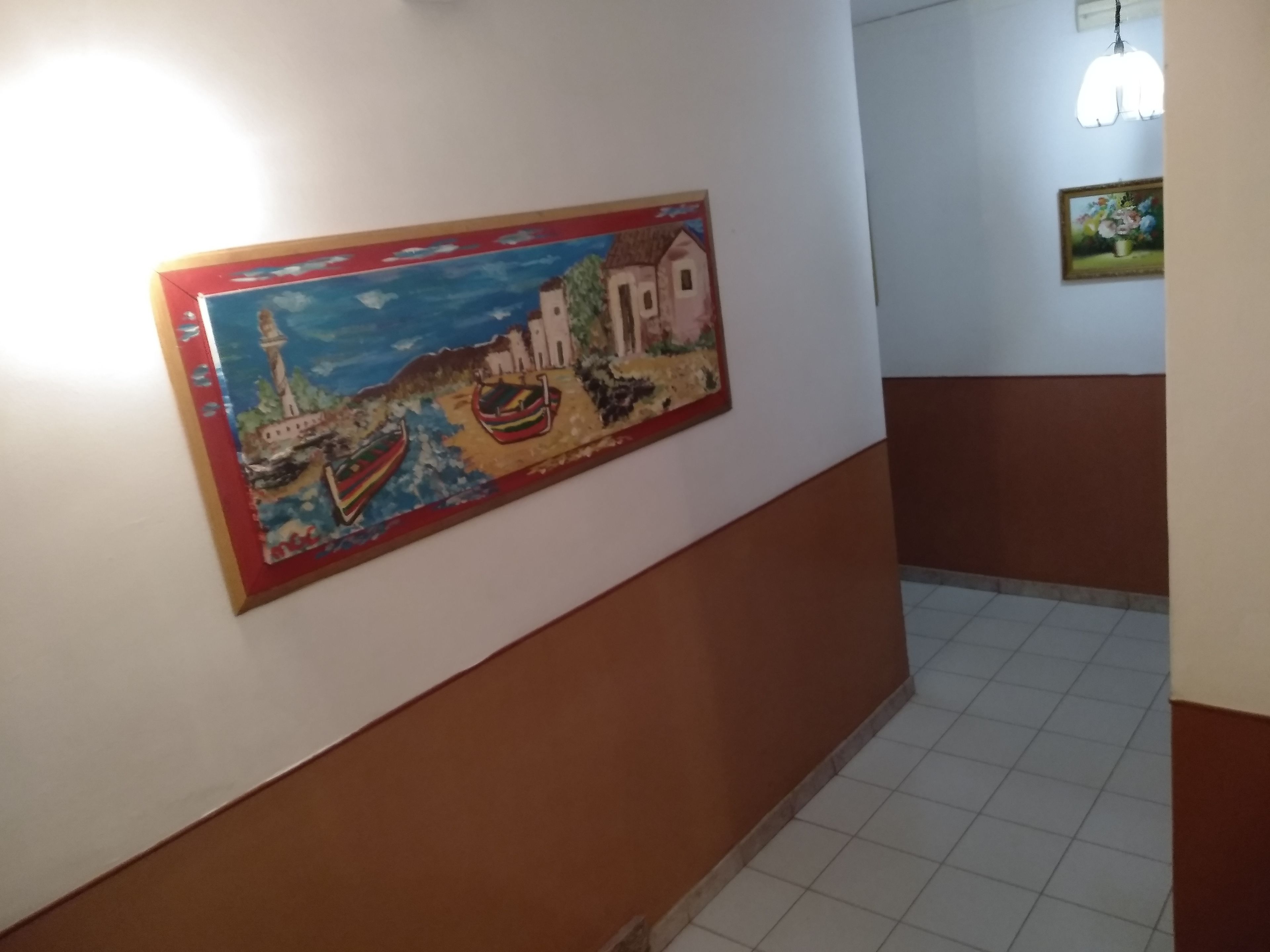 Un corridoio con un murale colorato che raffigura una scena costiera con barche e un faro.