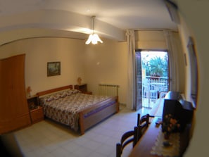 A bedroom with a bed, a desk, a chair, a radiator, and a window with a view of the outside. - Hotel Eliseo (Giardini Naxos)