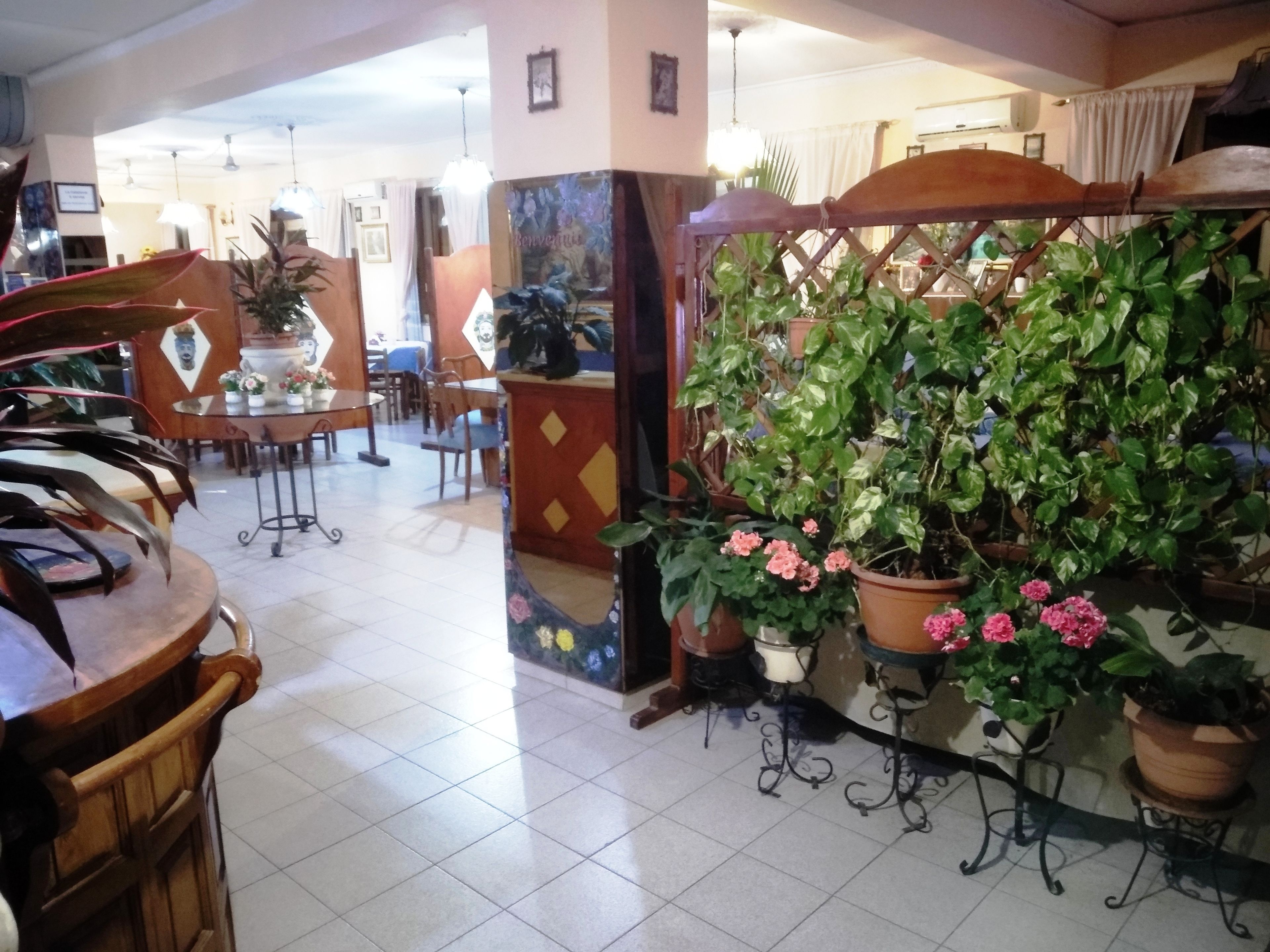 A hotel lobby with a tiled floor, wooden furniture, and potted plants.