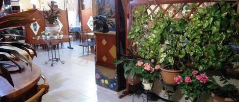 A hotel lobby with a tiled floor, wooden furniture, and potted plants.