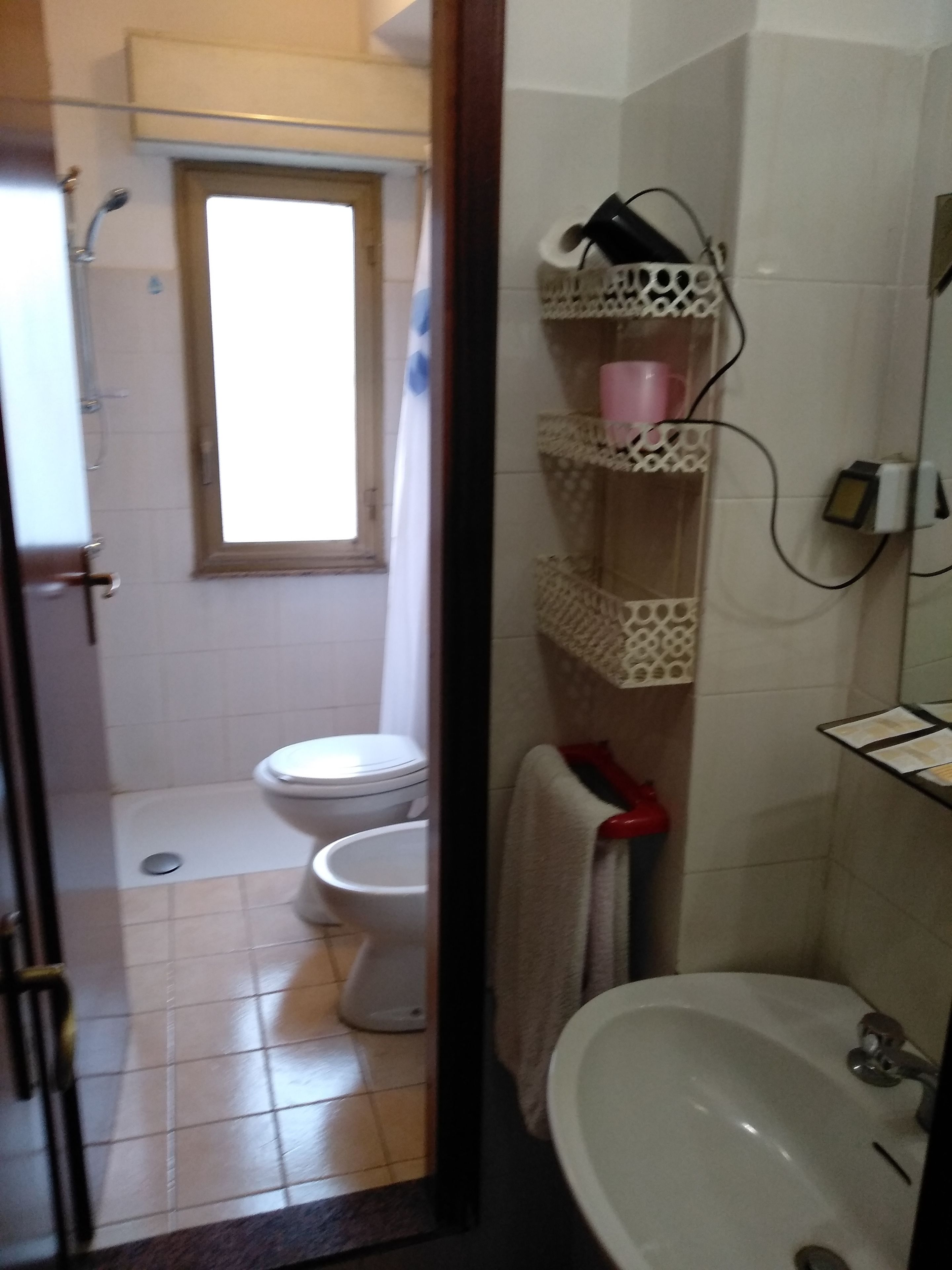 A bathroom with a toilet, sink, and shower. There is a window above the toilet and a towel rack with a towel hanging on it.