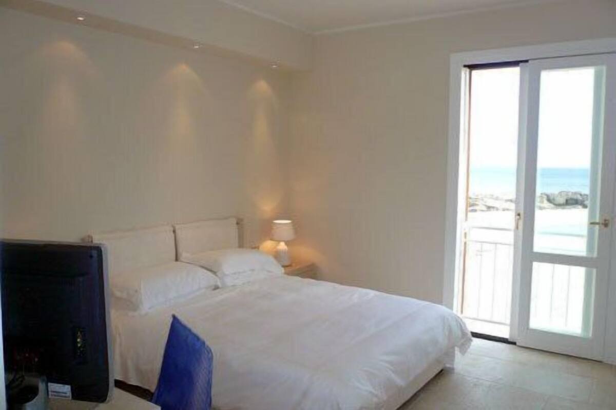 A hotel room with a bed, a TV, and a view of the sea through a door.