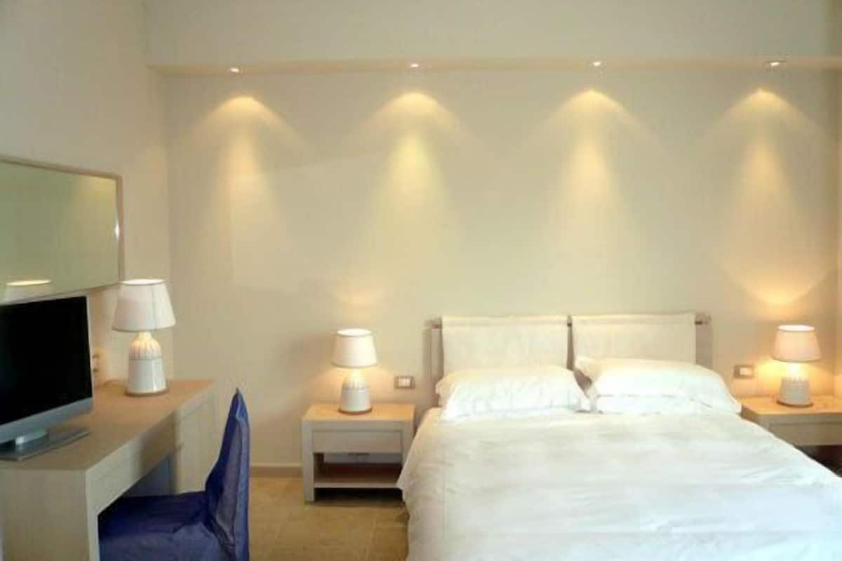 A hotel room with a bed, two bedside tables with lamps, a TV on a desk, and a chair.