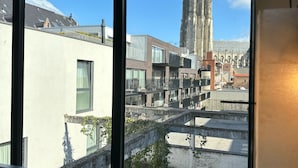 A view from a window overlooking a modern building with a tall tower, a courtyard with a fountain, and a balcony with a chair. - Hotel Vé (Mechelen)