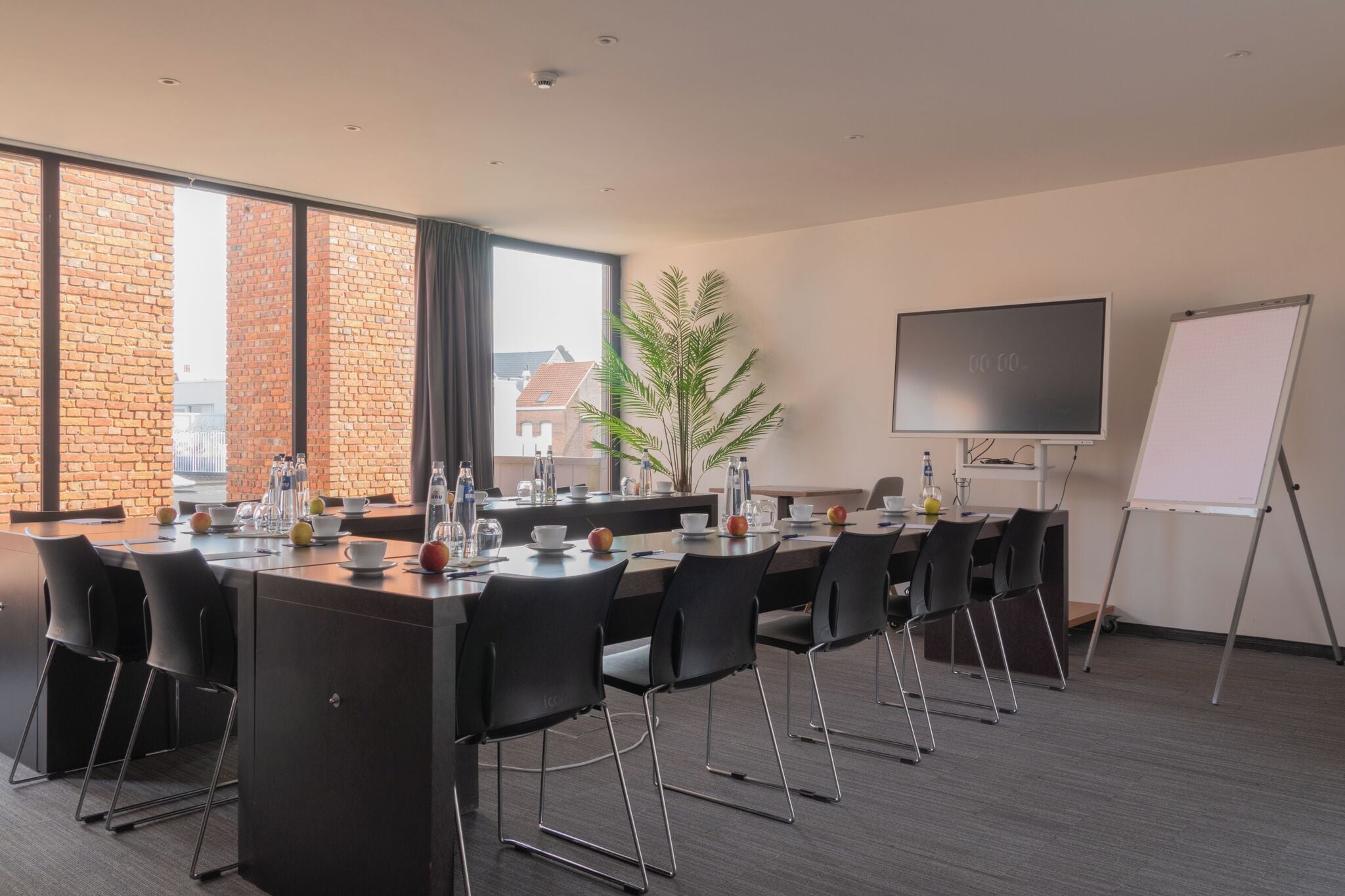 A conference room with a long table, chairs, a whiteboard, and a plant.