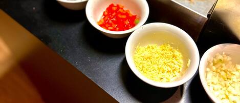 Una superficie de cocción con varios ingredientes en recipientes, incluyendo verduras picadas y especias.