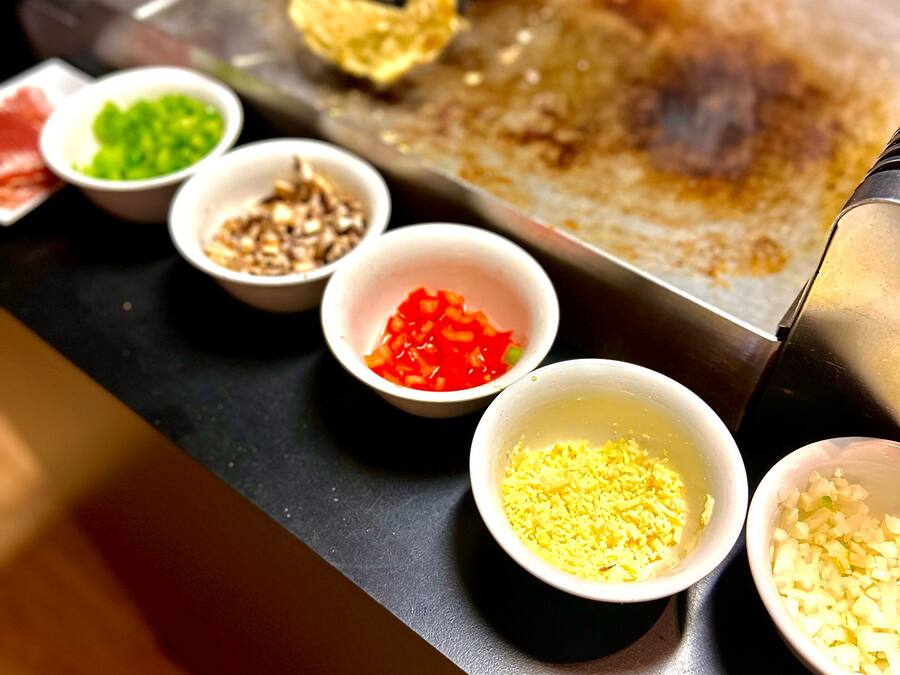 A cooking surface with various ingredients in bowls, including chopped vegetables and spices.