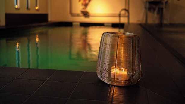 A candle in a woven container on a tiled floor near a pool. - Hotel Vé (Mechelen)