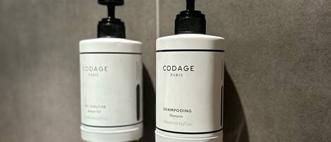 Two white CODAGE Paris shampoo bottles with black pumps on a tiled wall.