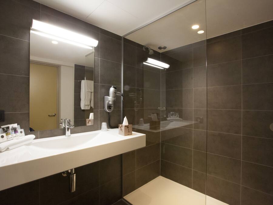 Een moderne badkamer met een grote spiegel, een witte wastafel en een douche met glazen wanden.