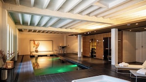 A modern indoor swimming pool with a jacuzzi, lounge chairs, and a wooden reception area. - Hotel Vé (Mechelen)