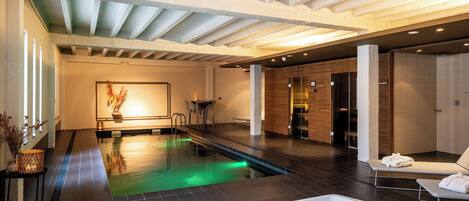 Una piscina interior moderna con jacuzzi, sillones de descanso y una zona de recepción de madera.