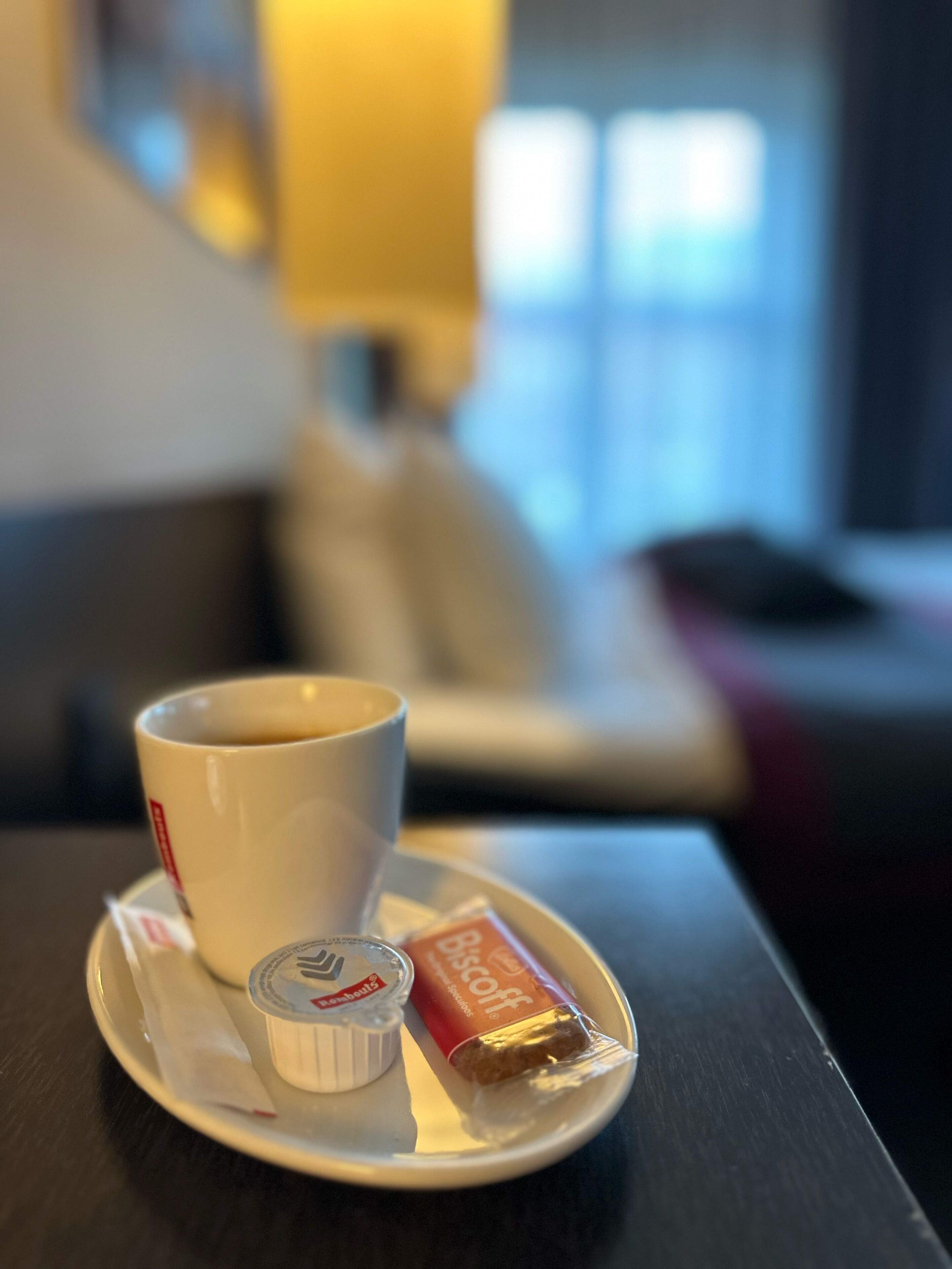 Una taza de café sobre un platito, con una galleta y un pequeño recipiente de crema, todo sobre una bandeja.