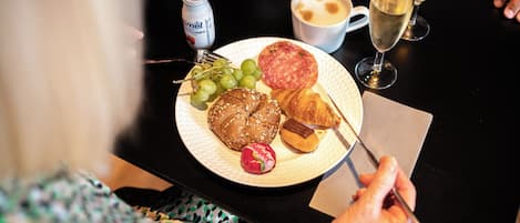 Un plato con alimentos como un croissant, una salchicha, uvas y un tomate cherry.